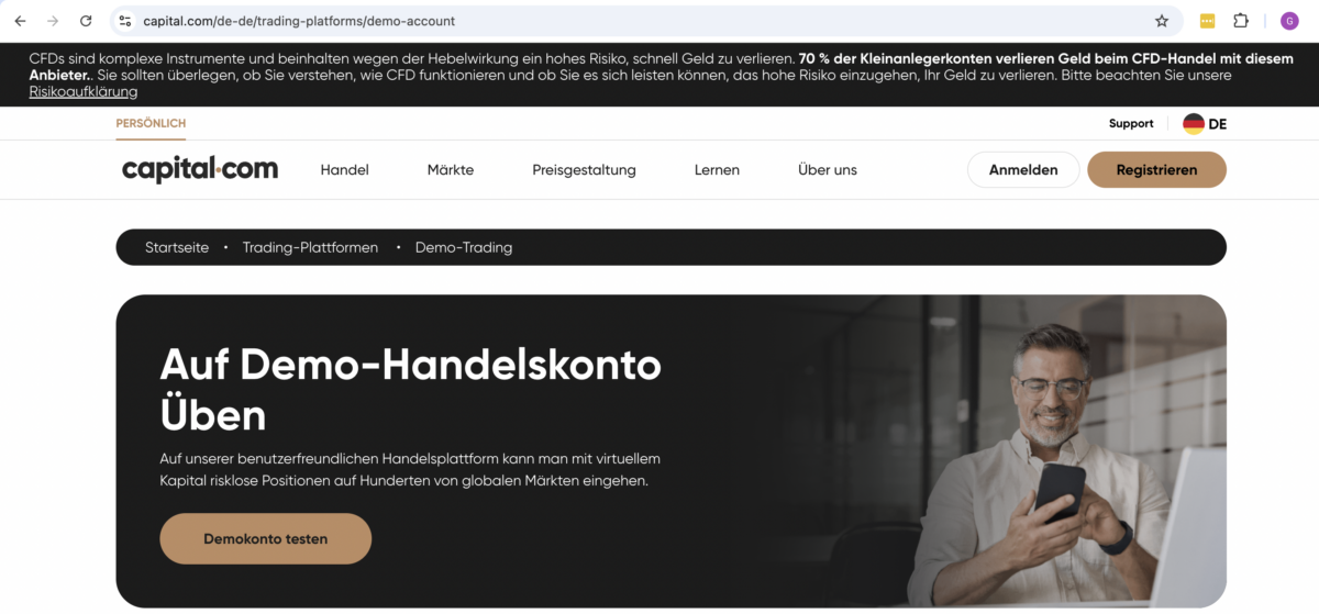 Trading Demokonto kostenlos und ohne Anmeldung (2025) Capital.com-Webseite mit einer Werbeanzeige für ein Demo-Handelskonto. Der Text lädt Nutzer dazu ein, auf der benutzerfreundlichen Plattform mit virtuellem Kapital zu üben. Links befindet sich ein brauner Button mit der Aufschrift 'Demokonto testen'. Rechts ist ein lächelnder Mann mit Brille zu sehen, der auf sein Smartphone schaut, während er an einem Laptop sitzt. Oben ist eine Risikowarnung zum CFD-Handel sichtbar
