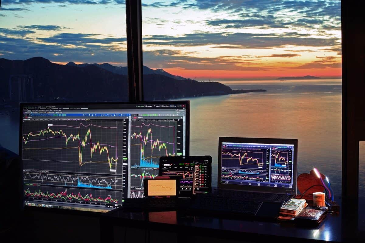 Der beste Trading-Computer: Alles, was Sie für den Einstieg wissen müssen Das Bild zeigt ein Trading Setup mit mehreren mobilen Geräten mit einem Ausblick aufs Meer im Hintergrund.
